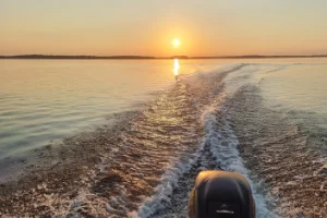 Aurinko paistaa Viinijärvellä. Aallokkoa syntyy veneestä. Moottori kuvassa.